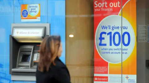 Woman wearing a dark coat looks at a sign that reads: Sort out your finances. We'll give you £100 when you switch your current account to us.