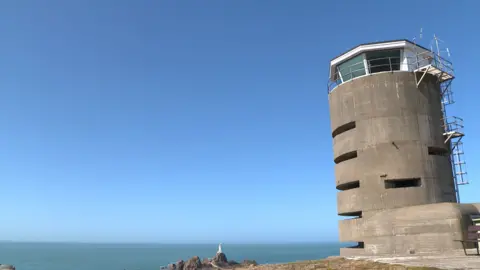 A large concrete gun emplacement from World War Two stands above a view to the sea with a lighthouse in the distance.