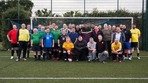 Roughly three dozen football players standing for a group photo in front of a goal