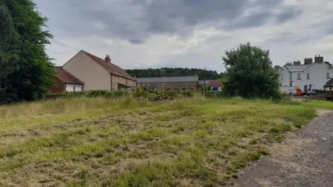 Andrew Melville  Houses in a rural area near grassland and a poorly paved path.