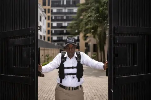 Olympia de Maismont / AFP A woman dressed in a security vest and chinos stands at the gates to private residence.