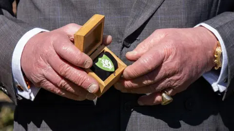PA Media A close-up photo of the King's hands, holding a small box with a green badge inside.