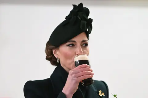 PA Media Princess of Wales wearing a green coat and green hat, sipping a half pint of Guinness.