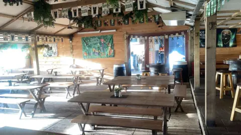 Connor Devine Tables and bench seats can be seen in a sunny room in the pub. St Patrick's Day decor is on the walls and roof. The walls are wooden panelled.