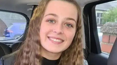 Family photo/PA Media Denii Reynolds with long brown hair looks at a camera while smiling in a car