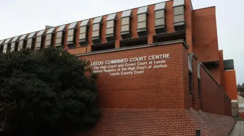 PA Leeds Crown Court - a redbrick building signposted as 'Leeds Combined Court Centre'. Underneath are the words: "The High Court and Crown Court at Leeds; District Registry of the High Court of Justice; Leeds County Court." A bush sits to the side.