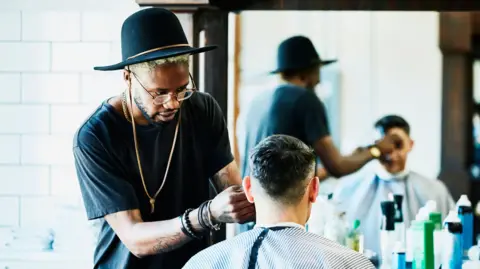 Getty Images Barber successful  a achromatic  t-shirt and wearing a chapeau  cutting different  man's hairsbreadth  successful  a barber shop