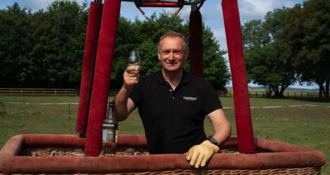 Sir David holding a glass of whisky in a hot air balloon
