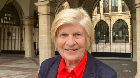 Nadia Lincoln/LDRS Sally Keeble is wearing a dark suit and red shirt. She has short blonde hair. 