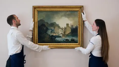 Two Sotheby's workers, one man and one woman, both wearing white smart shirts, gloves and dark aprons, hold the painting in a frame as though they are mounting it to a wall. It is housed in a golden gilt frame, and mostly consists of dark blues, greys and greens. 