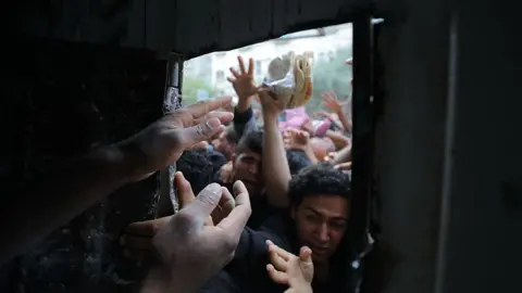 Getty Images Displaced Palestinians reach through a bakery window as they try to obtain bread after a limited amount of flour entered the Gaza Strip, where humanitarian aid has been severely restricted since March 2, in Nusseirat Refugee Camp, Gaza on May 22, 2025.