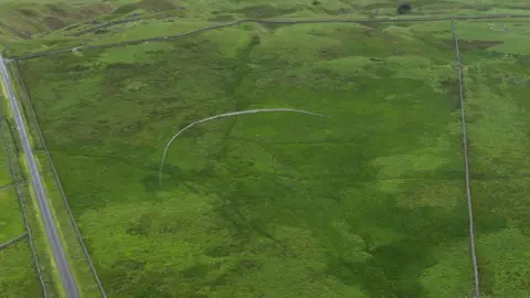 The Environment Agency An aerial view of a timber fence which has been built in the middle of a field. The fence has been built in a crescent shape.