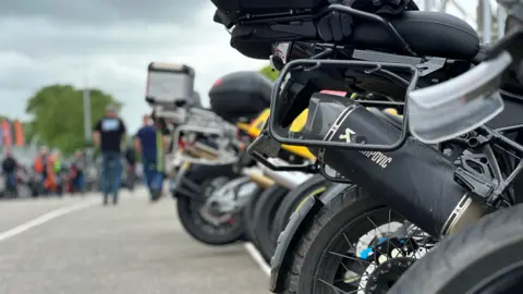 The rear of a row of bikes lined up. Some have storage boxes on the back.