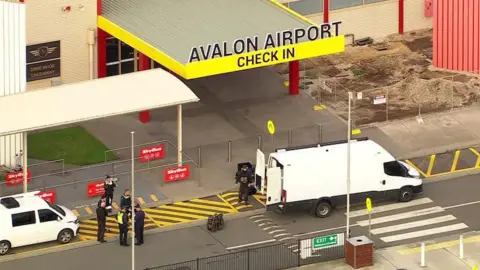 The entrance of Avalon airport with a white van and police officers standing in front of it