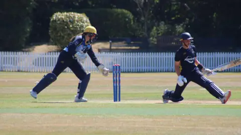Libby Thomas Libby, with a long brown ponytail under her yellow helmet takes the ball in her left glove as she prepares to whip off the bails 