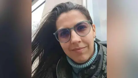 Family handout Vitória is looking at the camera up close. She is wearing a blue turtle neck jumper, a khaki or dark-coloured coat, has glasses on, and has brown hair.