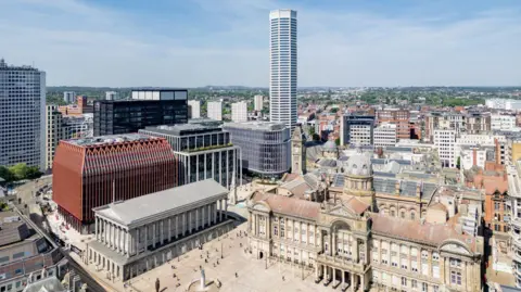 The Octagon Birmingham A drone shot of The Octagon towering over Birmingham's Chamberlain Square. It is gleaming white and has eight sides. There is a crown on top. It is a clear day with few clouds in the sky. We can see Birmingham's old-fashioned architecture, including its council house, clashing with the modern design of The Octagon. Because we are higher up we can see even further across the city. There are buildings as far as the eye can see. 