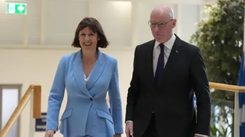 PA Media Rachel Reeves and John Swinney walking together. Both are smiling as the Chancellor visited Scotland.