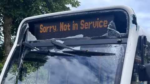 BBC A bus with a smashed windscreen, electronic sign, and chassis. Electronic sign says: Sorry, Not in Service.