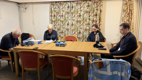 Four people sat around a brown table praying. 