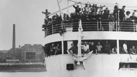 The Empire Windrush arriving at Tilbury Docks in 1948 with people leaning over the decks off the side of the boat