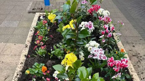 Staffordshire Police A colourful set of flowers in a raised flower bed, in a wooden container, with a pavement in the background.