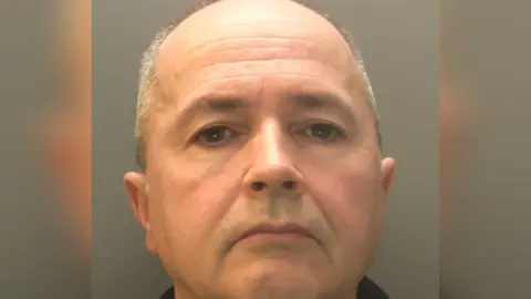 A mugshot of a man with grey hair, looking directly at the camera.