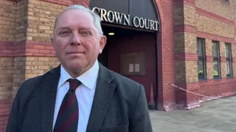 Derek Bennett: a grey haired man wearing a grey jacket and red tie outside a red-and-brown brick building. The words "crown court" are written above the entrance to the building in capital letters.