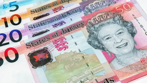 The face of Queen Elizabeth II is seen on a £50 note with a £20 and a £10 note behind it. They are headed States of Jersey. 