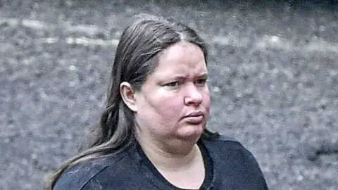 Solent News and Photo Agency Jeniffer Rocha, a woman with long, straight hair who wears a dark top. She has a slight frown in this zoomed-in photograph taken at some distance outside court.