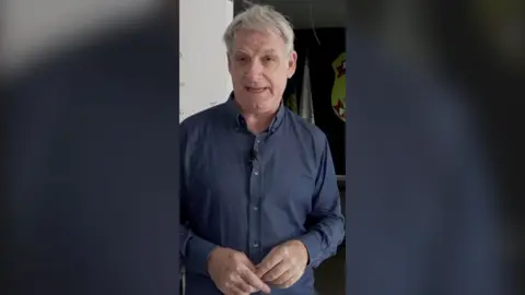 Jonathan Head looks at the camera. He wears a blue long-sleeve shirt. 