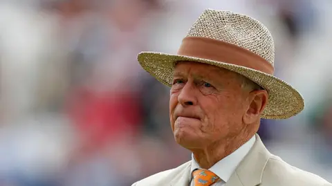 Sir Geoffrey Boycott, pictured wearing a boater hat and beige suit.