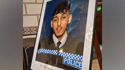 Jenny Kirk/BBC A photo of PC Faizaan Najeeb, pictured in uniform, is printed and framed. It is fixed to an easel in a hall.