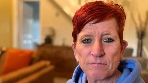 Woman with short red hair and blue hoodie sat in living room