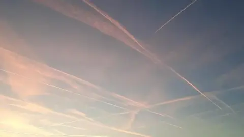 Peach and gold-coloured vapour trails criss-crossing the blue sky