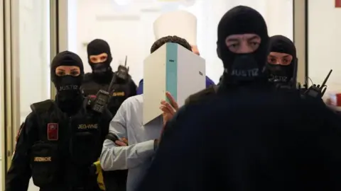 Reuters Two men suspected of being Islamic State (IS) supporters, who were planning an attack on Taylor Swift's Vienna concert in 2024, are escorted by security personnel as they arrive in a courtroom for their trial in Wiener Neustadt