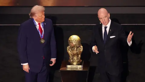 PA Media US President Donald Trump standing on stage being presented with the inaugural Fifa Peace Prize award by Fifa president Gianni Infantino