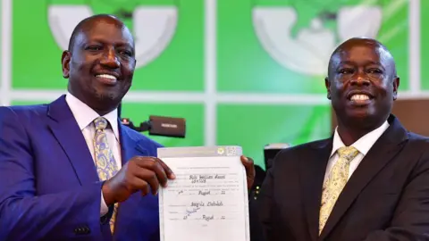 AFP Both wearing suits, William Ruto stands with Rigathi Gachagua holding the election certificate between them in an archive photo from 2022.