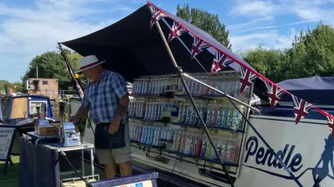 Patrick Creaven on his sweet shop boat - with the side open to reveal jars of sweets, and a cash desk in front.