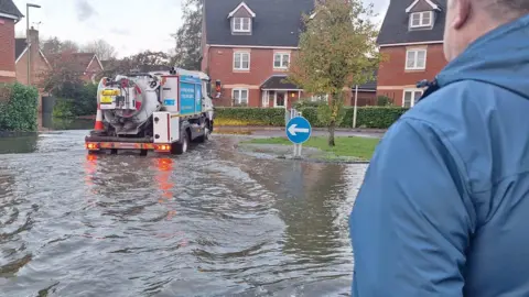 Keith Underwood A thames water lorry pumping water out of a flooded street whilst a man in a blue coat watches on.