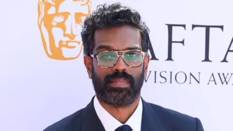 Getty Images Romesh Ranganathan in a suit standing in front of a white backdrop.