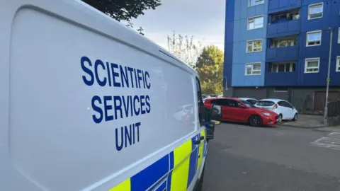 Emma Baugh/BBC A Scientific Services van parked outside a block of flats