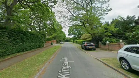 A streetview of a residential area. There is a black car and grey car parked on the side.