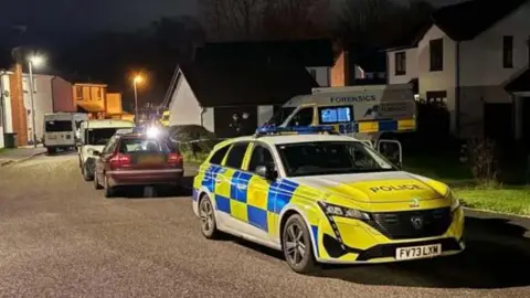 A police care and forensics van are parked in a street at night time