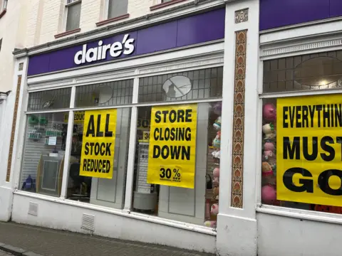 The front of a Claire's store with signs promoting a closing-down sale with slogans such as 'everything must go' 