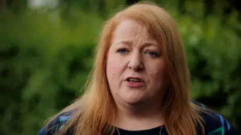 PA Media Naomi Long - a woman with medium-length ginger hair wears a floral top.