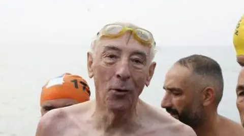 Getty Images Mr Read stands up in open water at the end of a race. His goggles sit on top of his forehead. He is surrounded by other swimmers. 
