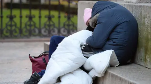 Two homeless people sleeping on a stone or concrete step, under a duvet with no case on it.