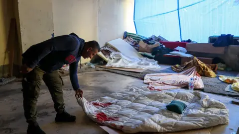 EPA A displaced Lebanese man holds a blood-stained duvet following an Israeli strike on the Ramada Plaza hotel in Beirut's Raouche district, during which his children were injured by shrapnel (8 March 2026)