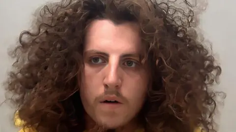 A mugshot of a man with a lot of curly, shoulder-length hair.